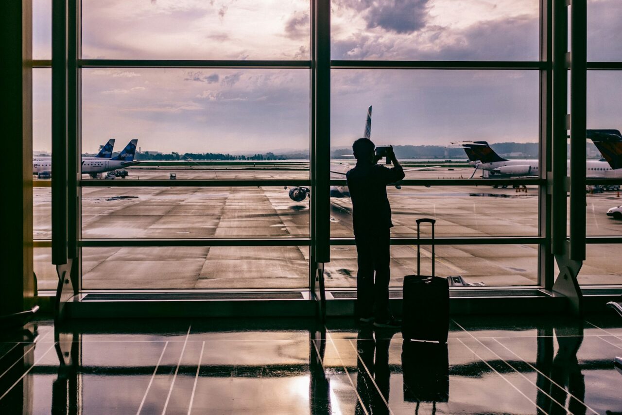 silhouette of person standing in front of glass while taking photo of plane at airport