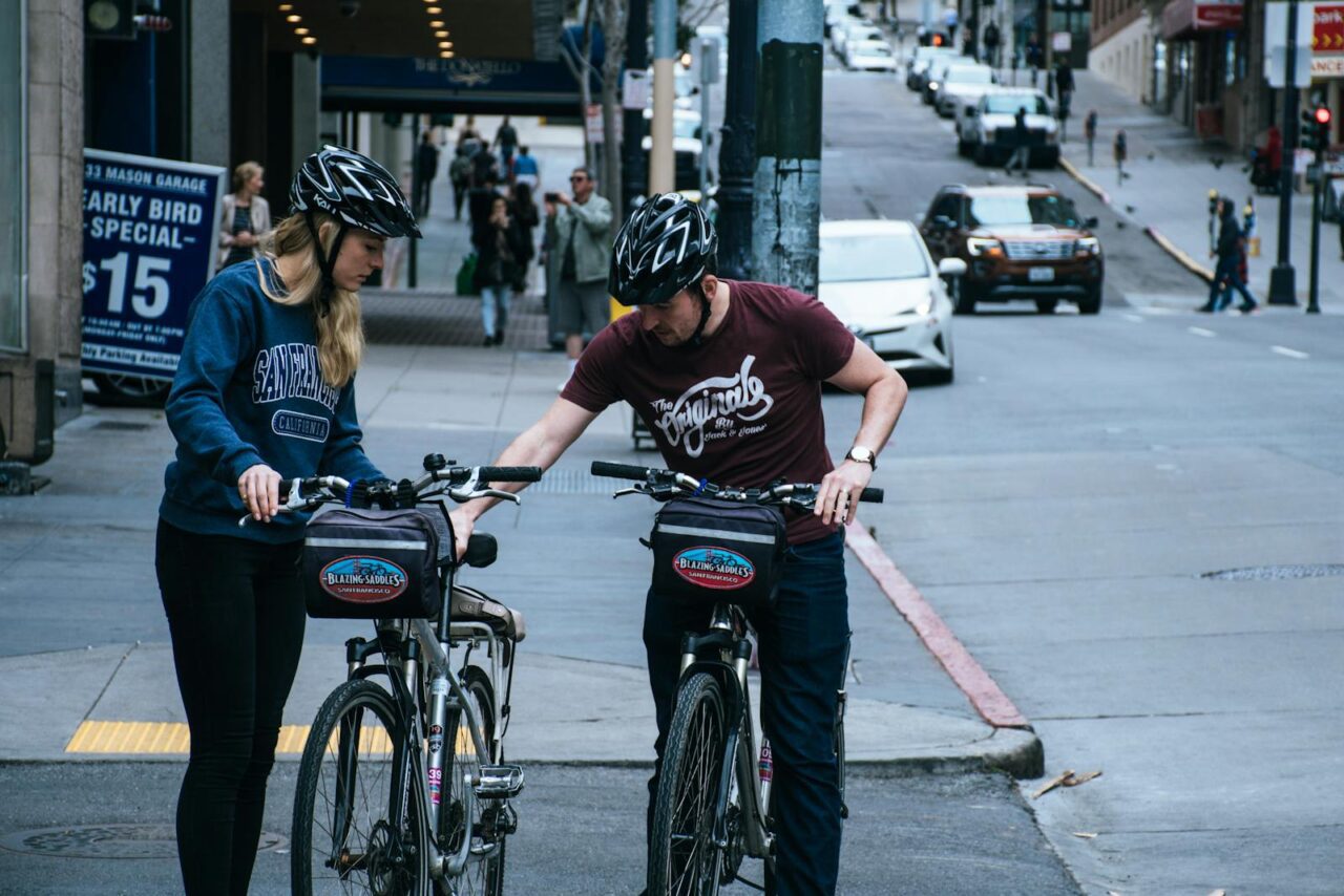 Two cyclists pause on a street to plan their route in a busy urban environment.