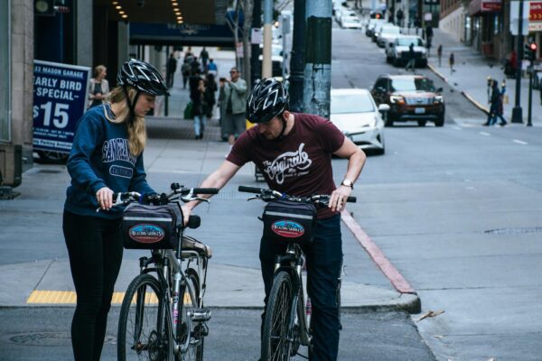 Two cyclists pause on a street to plan their route in a busy urban environment.