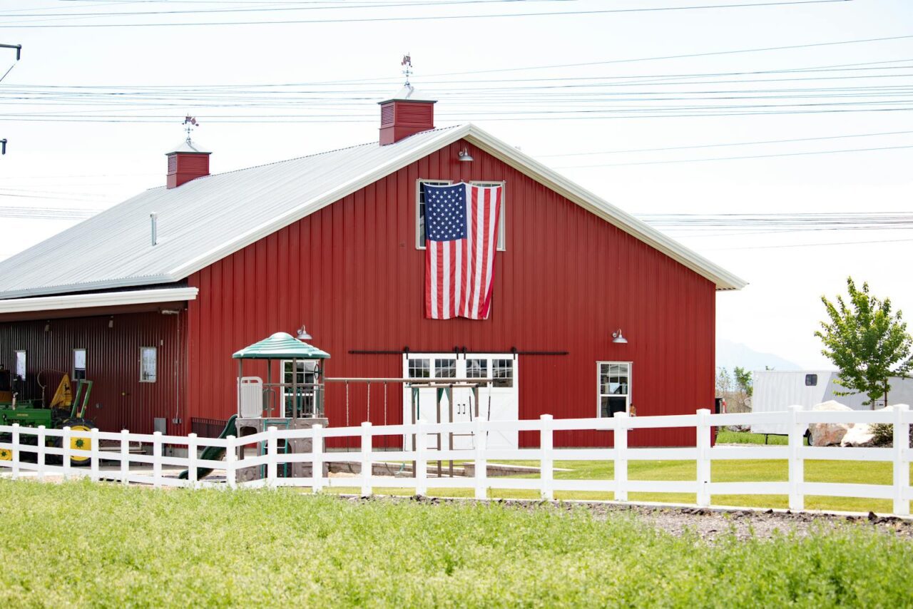 A classic red barn with an American flag, surrounded by fencing in a rural landscape.