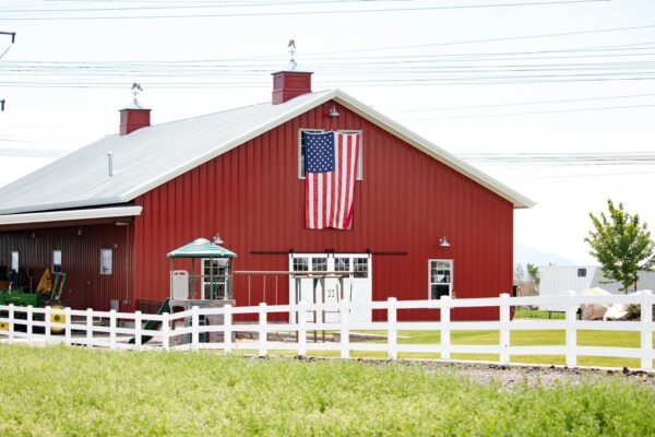 A classic red barn with an American flag, surrounded by fencing in a rural landscape.
